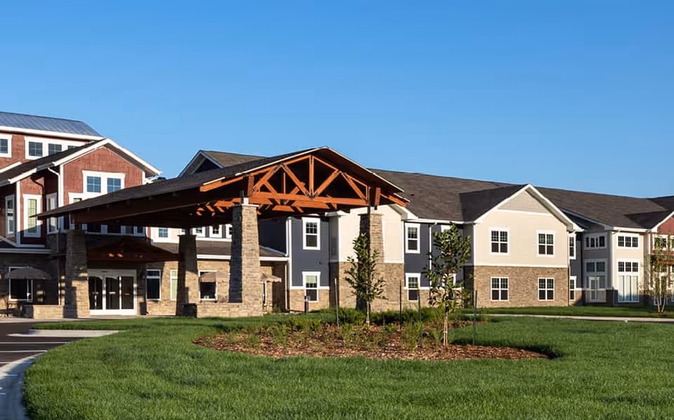 Senior living facility exterior featuring a covered entrance and landscaped lawn under a blue sky.