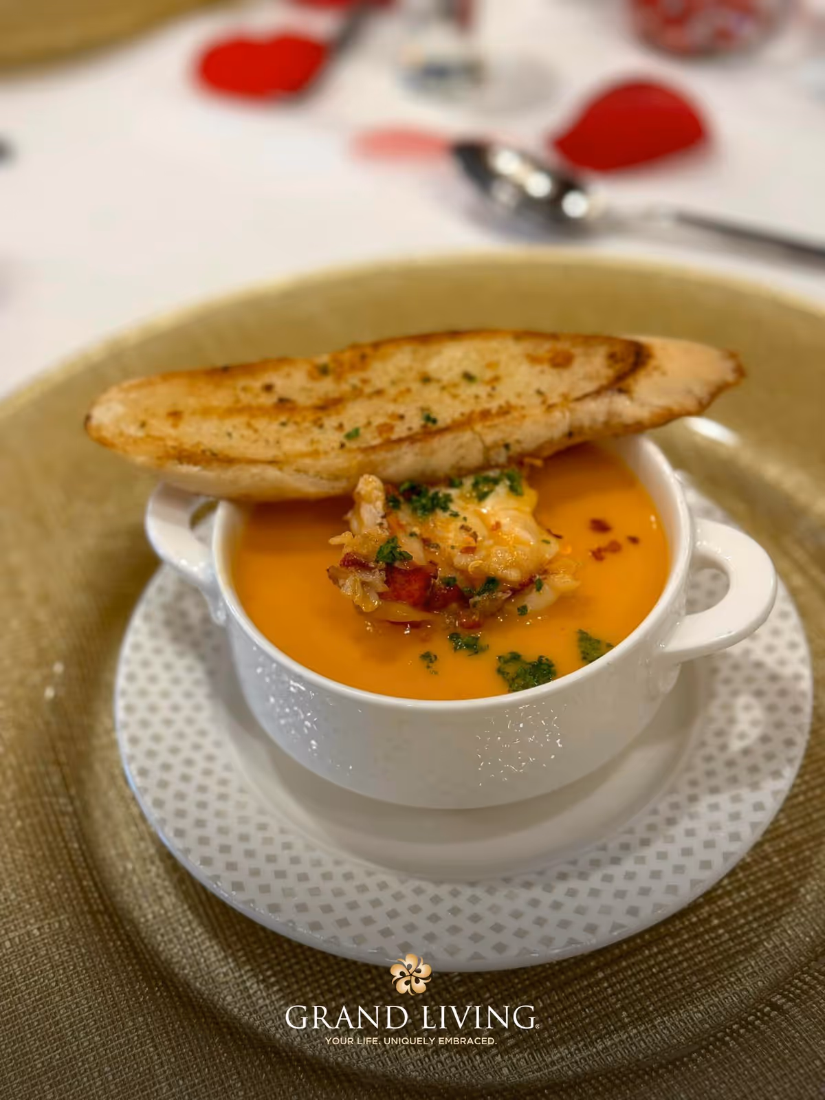 A bowl of creamy soup topped with lobster and herbs served with a toasted bread slice on a white plate.