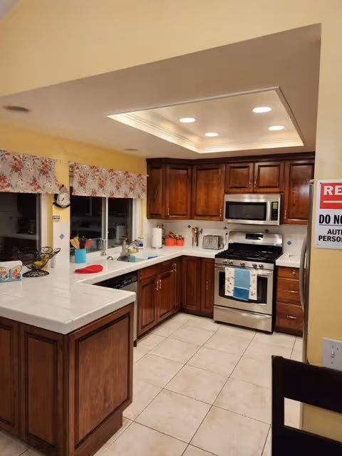 Bright kitchen with wooden cabinets, white tile countertops, a stainless steel stove and microwave, and a central island.