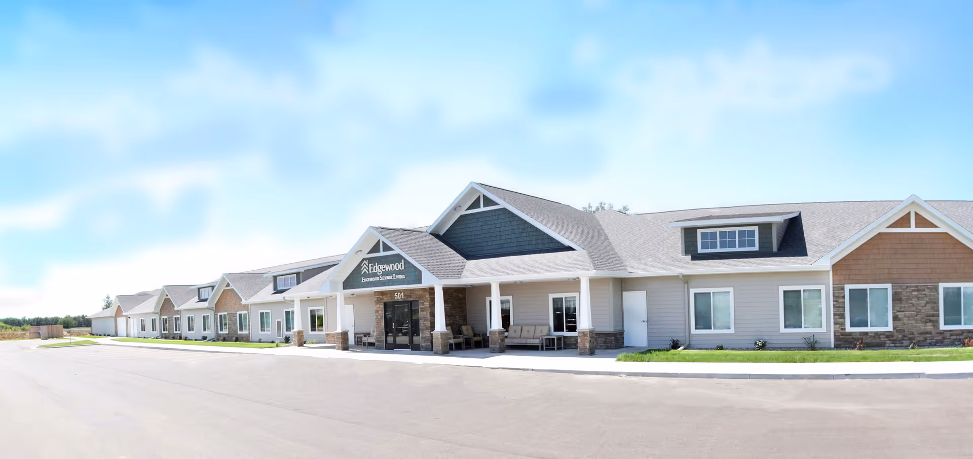 Exterior view of Edgewood Mitchell, a single-story senior living facility with a large covered entrance, multiple windows, and a paved driveway under a partly cloudy sky.