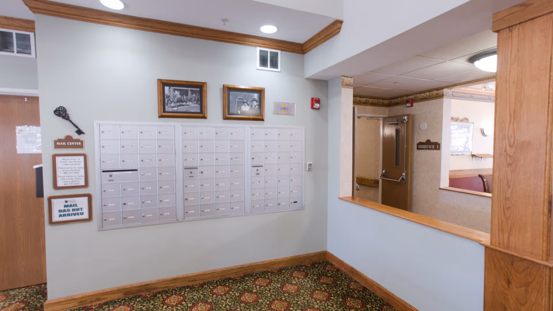 Interior mail center area with a wall of resident mailboxes, framed photos, and a wood-trimmed hallway.