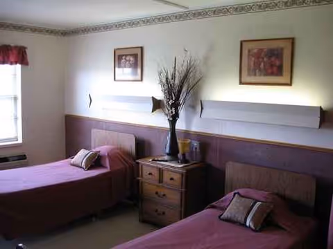 Two twin beds with purple bedding, nightstand, and wall decor in a shared senior living bedroom.