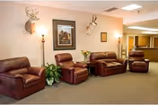 A lounge area with several brown leather armchairs and a loveseat against a wall decorated with framed art and mounted deer heads.