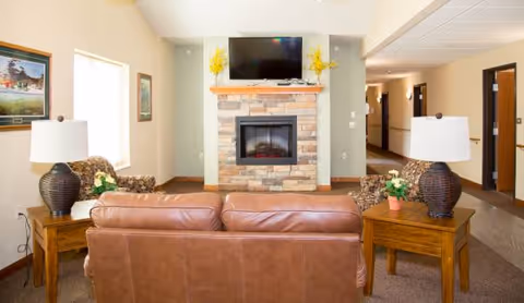 Cozy living room with stone fireplace, mounted TV, brown leather sofa, and side tables.