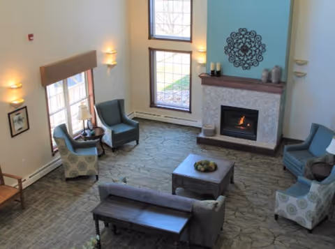 Cozy senior living room with a fireplace, blue armchairs, sofa, and large windows.