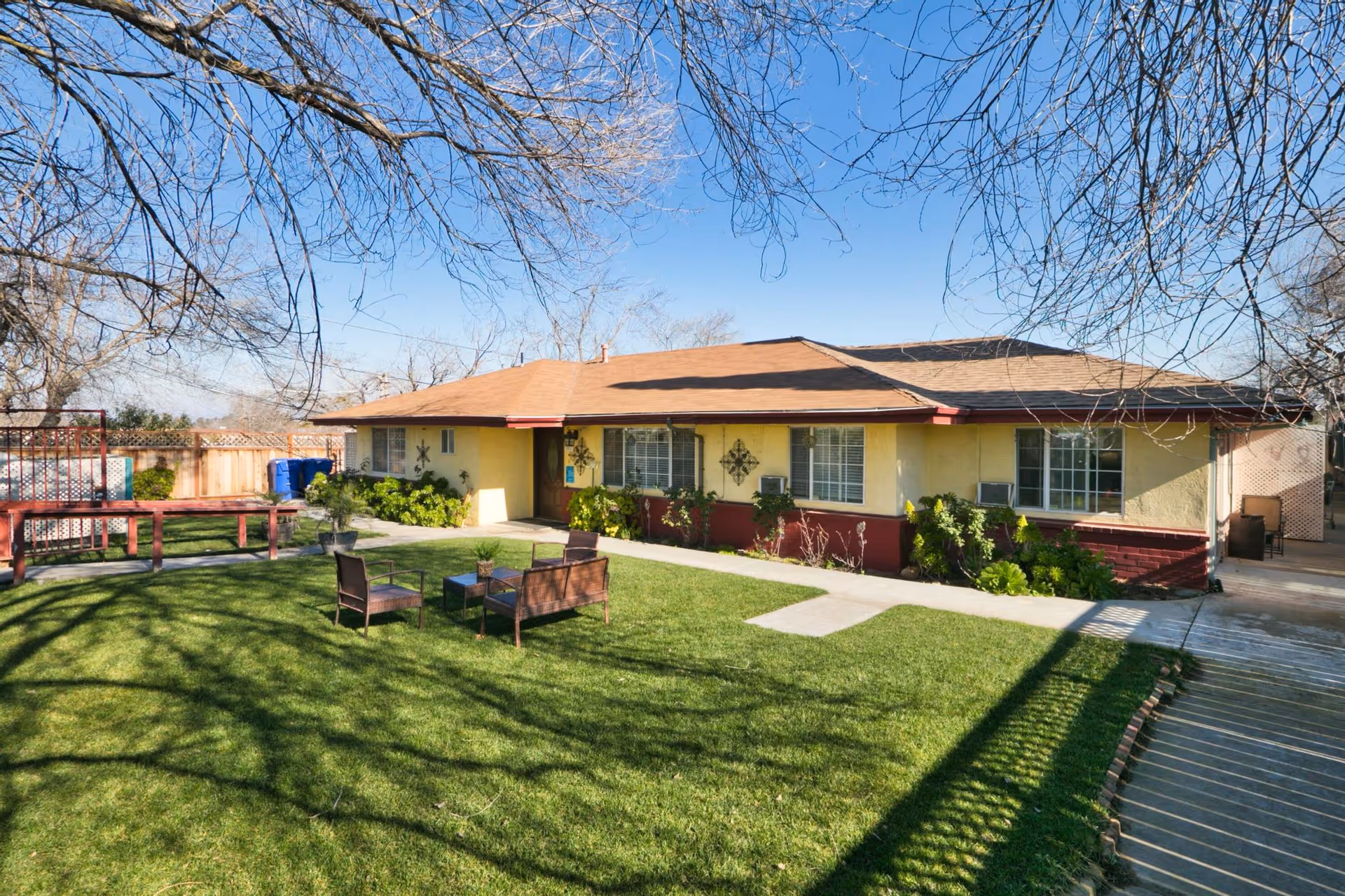 Single-story yellow building with a manicured lawn, outdoor seating, and leafless trees in front.