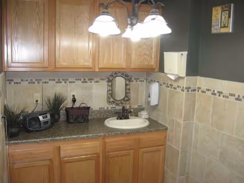 Wood cabinets and a sink vanity in a tiled bathroom with bright overhead lights.