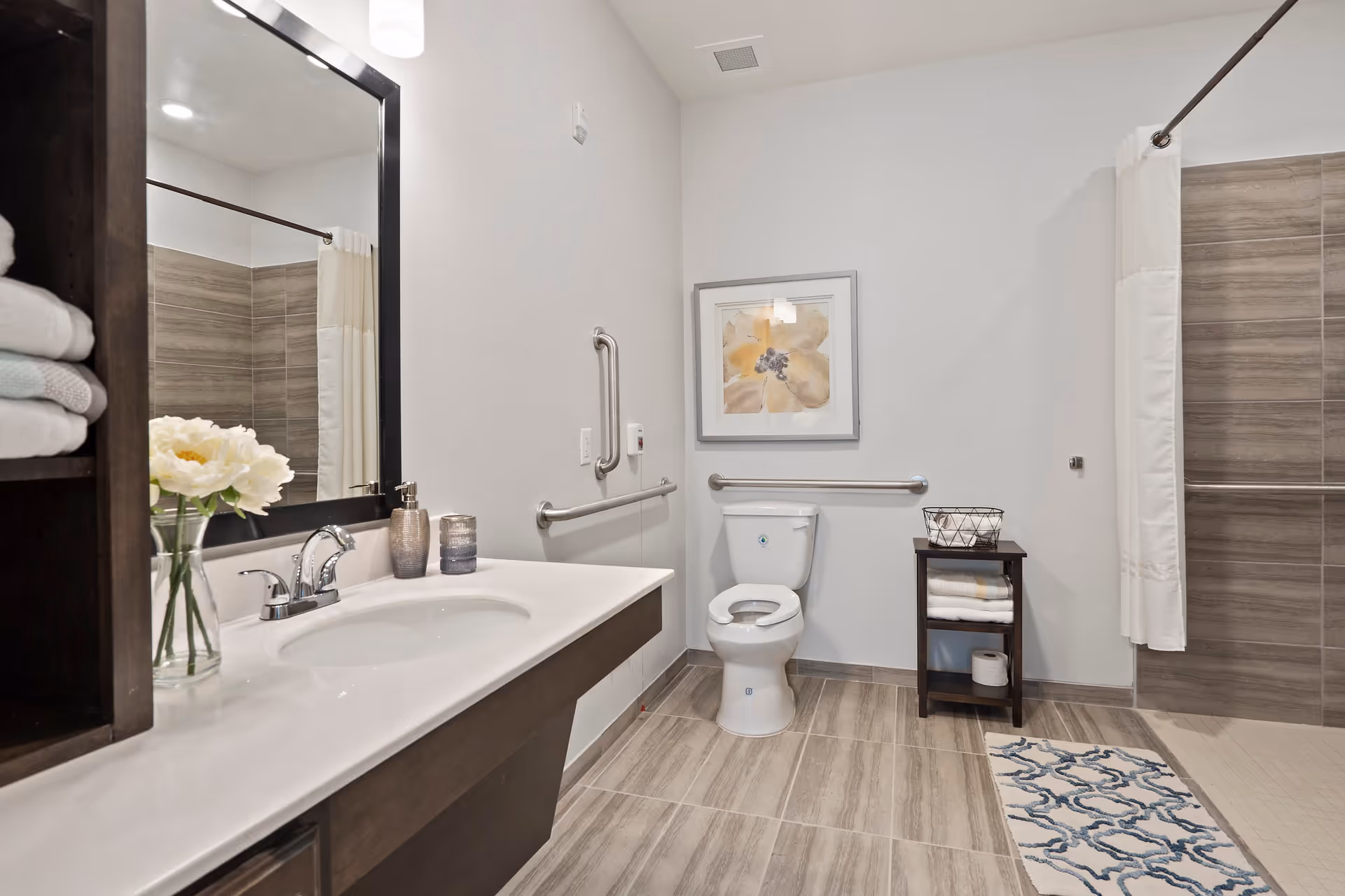 Accessible modern bathroom with a sink and mirror on the left, a toilet with grab bars in the center, and a walk-in shower with curtain on the right.