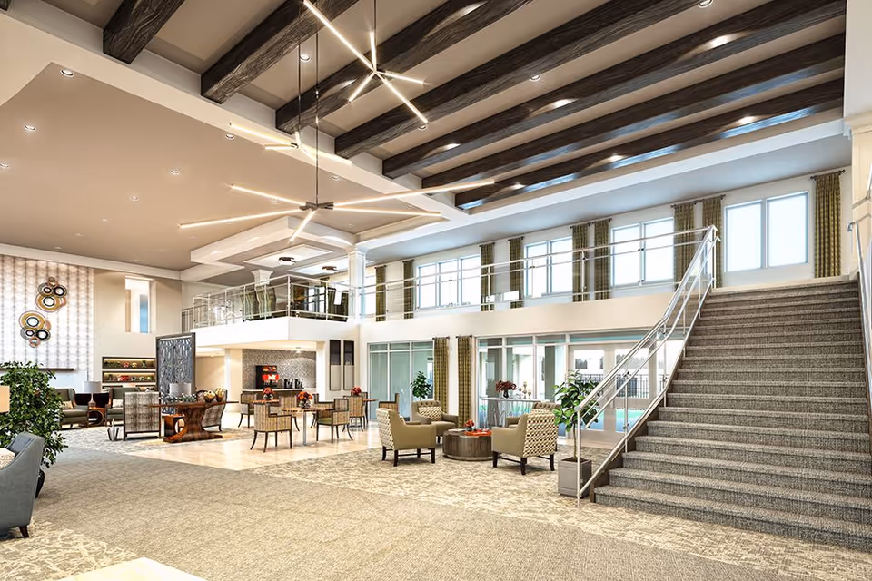 Spacious and modern senior living facility common area with high ceilings featuring exposed wooden beams and contemporary lighting. The room includes multiple seating arrangements with armchairs and tables, a staircase with a metal railing leading to an upper level with large windows and green curtains, and decorative plants throughout. The area is well-lit with natural light coming through the windows.