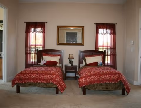 Twin beds with red bedding and a nightstand between them in a beige bedroom.