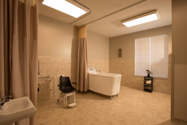 Accessible bathing room with a walk-in tub, shower chair, privacy curtains, sink, and tiled walls and floor.