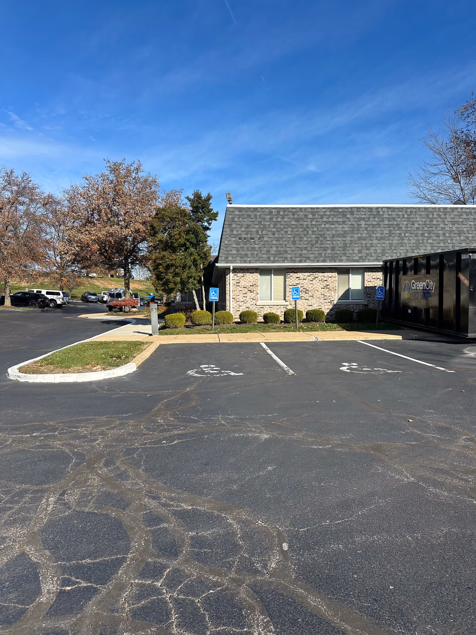 Parking lot with marked handicap spaces in front of a single-story brick building and trees under a blue sky.