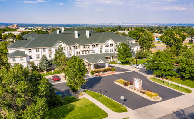 Aerial view of the Woodlake Legacy Senior Living three-story building with a covered entrance, parking lot, and surrounding trees and lawns.