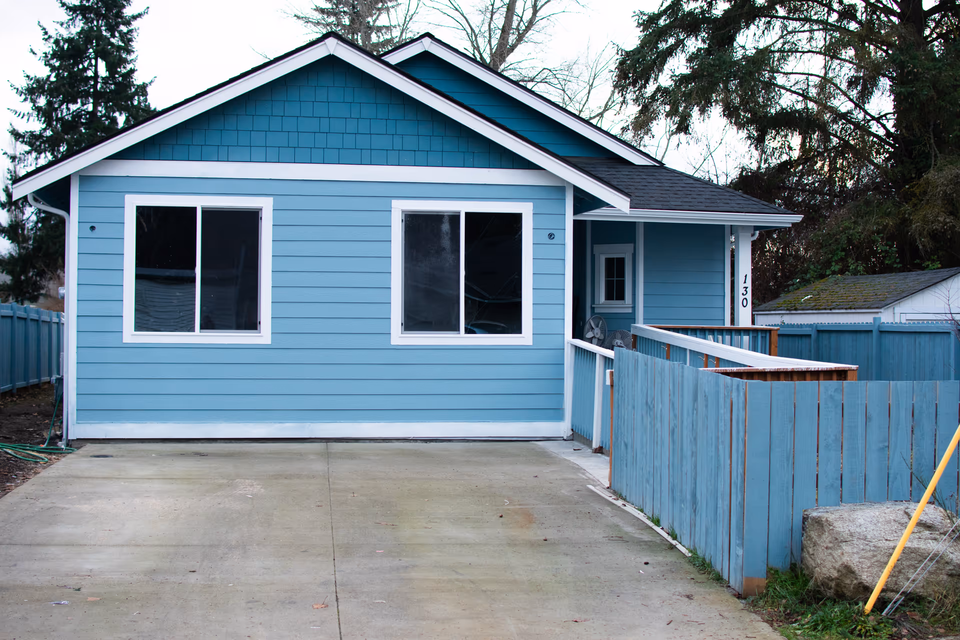 Front view of a small blue single-story house with a concrete driveway and a fenced ramp to the entrance.