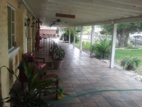 Covered outdoor walkway of a senior living facility with chairs, potted plants, and garden view.
