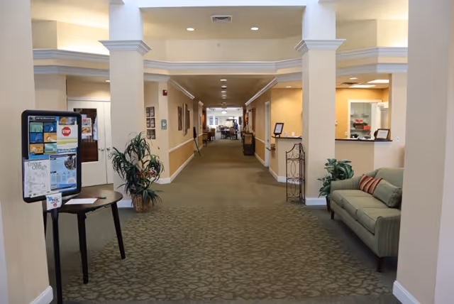 Carpeted lobby hallway with seating, plants, and a bulletin board leading to common areas.
