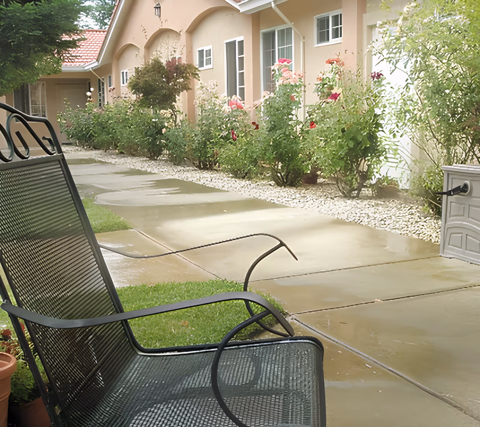 A wet paved courtyard with metal patio chairs, flower beds, and the exterior of a single-story senior living building.