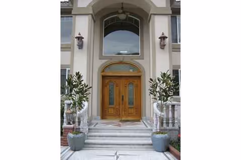 Front entrance of a building with wooden double doors, arched window, and potted plants.