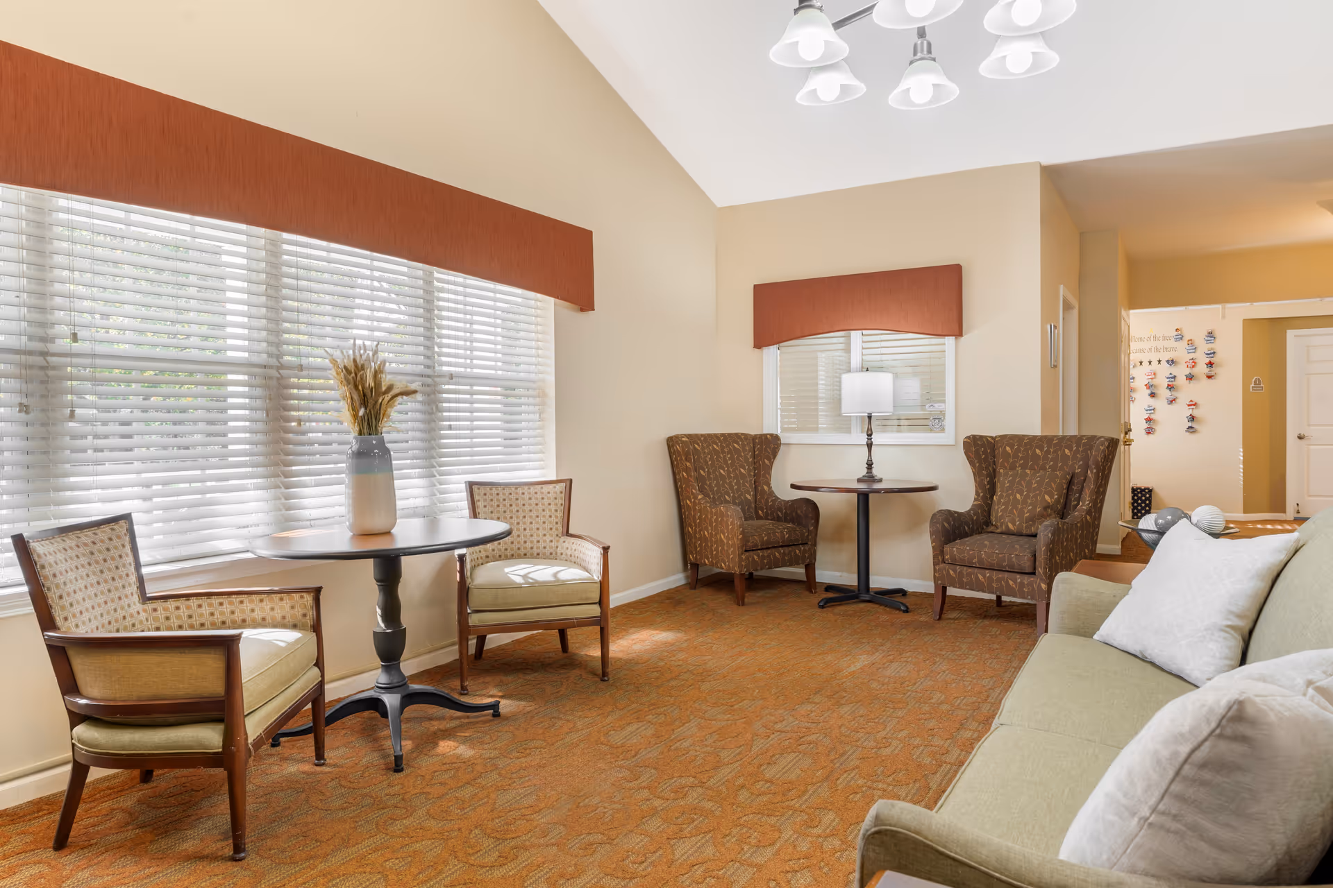 Bright seating area with armchairs, small round tables, a sofa, and a large window with blinds.