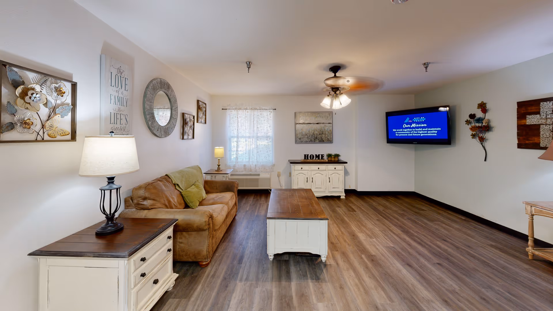Bright common living room with a sofa, coffee table, side tables, wall-mounted TV, and decorative wall art.