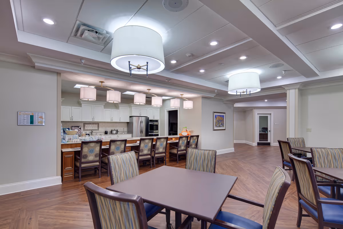 Spacious dining area with tables and chairs facing a serving counter and open kitchen with pendant lights.