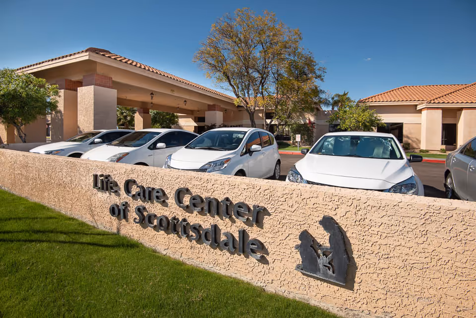 Entrance and sign for Life Care Center of Scottsdale in front of a stucco building with parked cars under a covered drive.