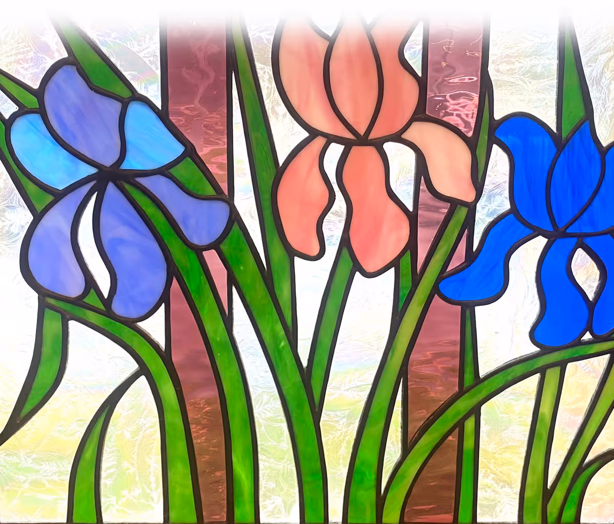 A stained glass window featuring three large flowers with green stems and leaves. The flowers are colored purple, pink, and blue, set against a textured background with vertical reddish-brown and clear glass panels.