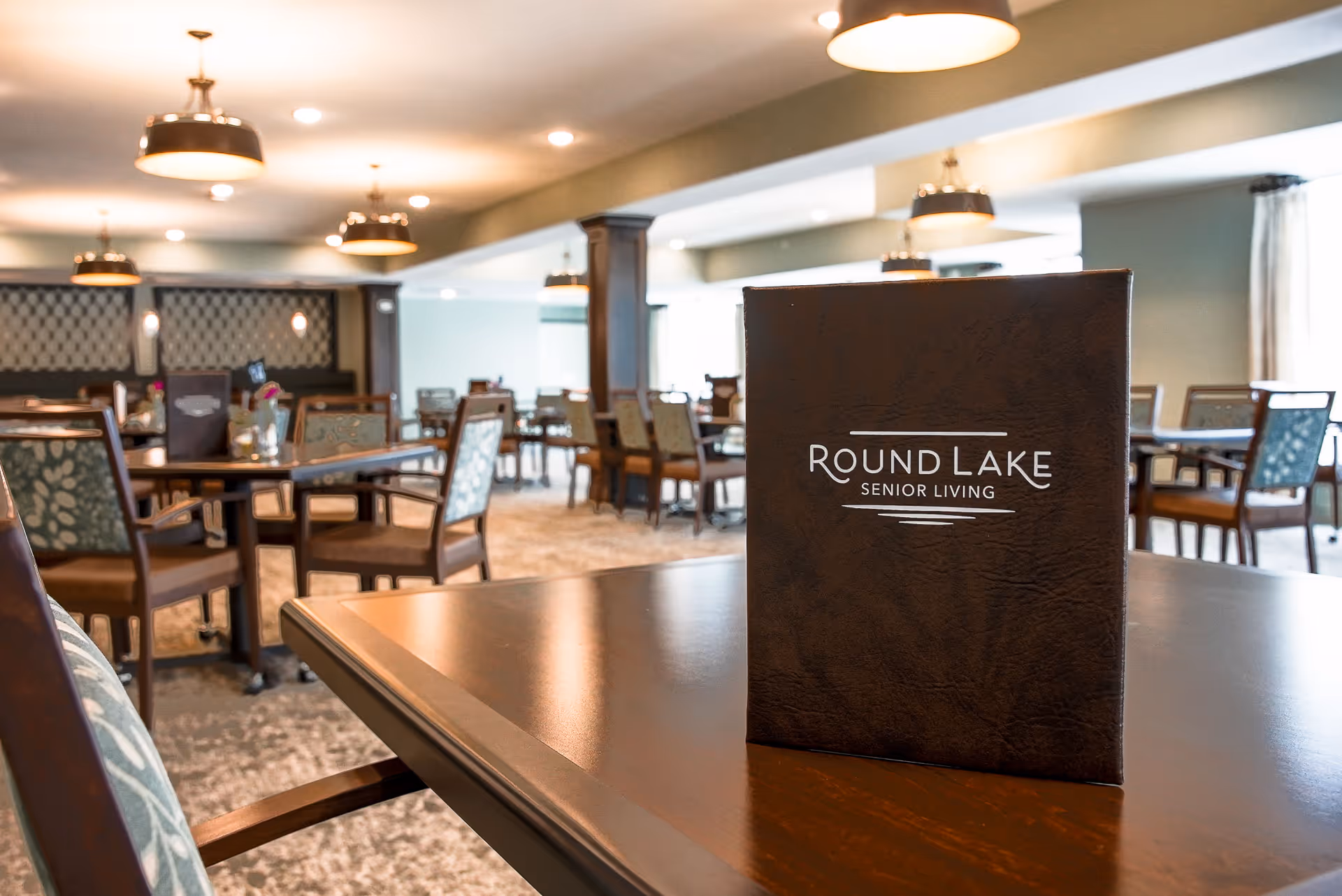 Dining room with tables and chairs and a "Round Lake Senior Living" menu standing on a table.
