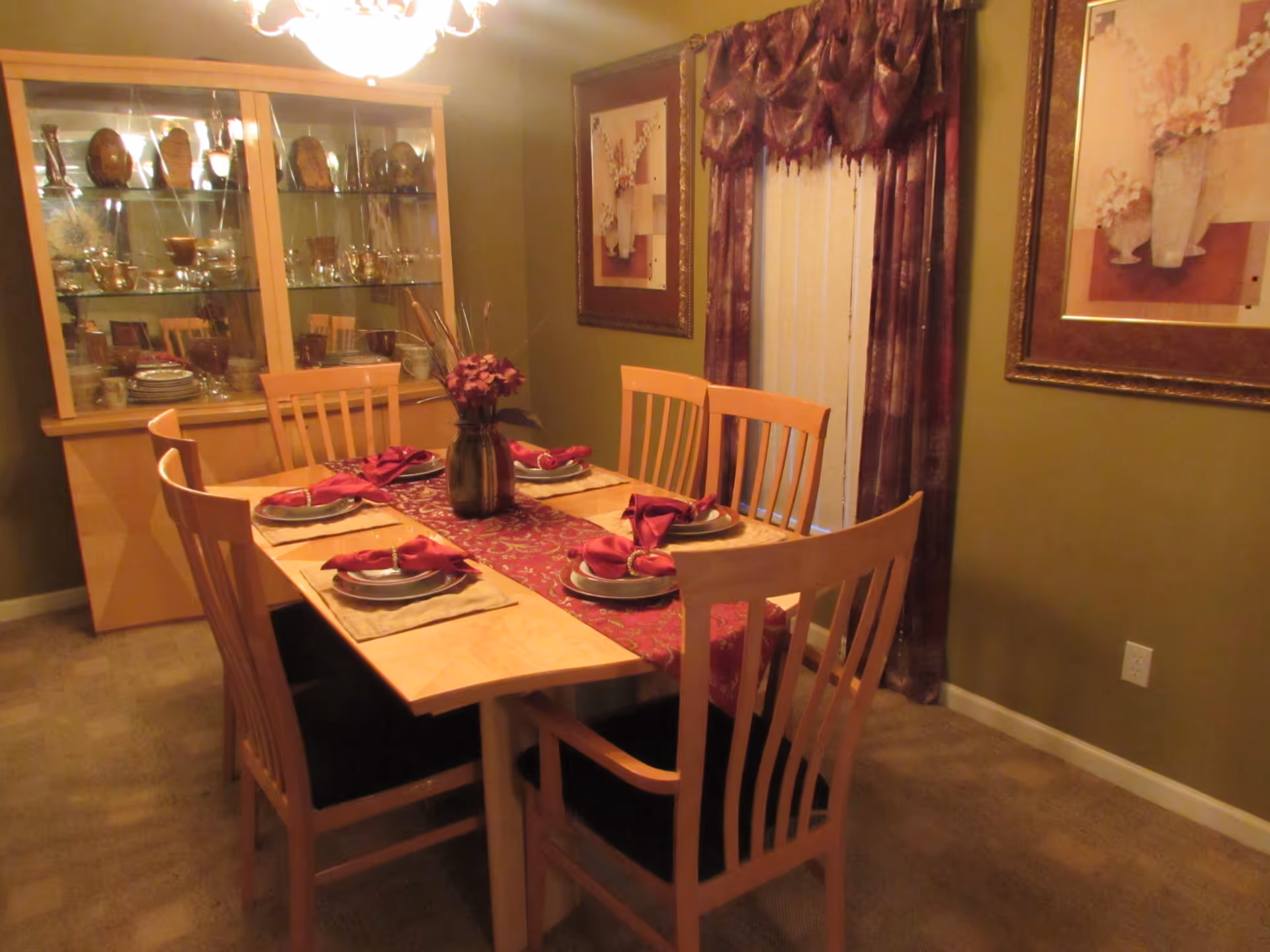 Dining room with a wooden table set for six, a vase centerpiece, and a glass-front china cabinet.