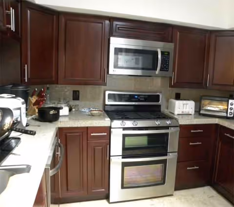 Modern kitchen with dark wood cabinets, stainless steel stove, microwave, and appliances.