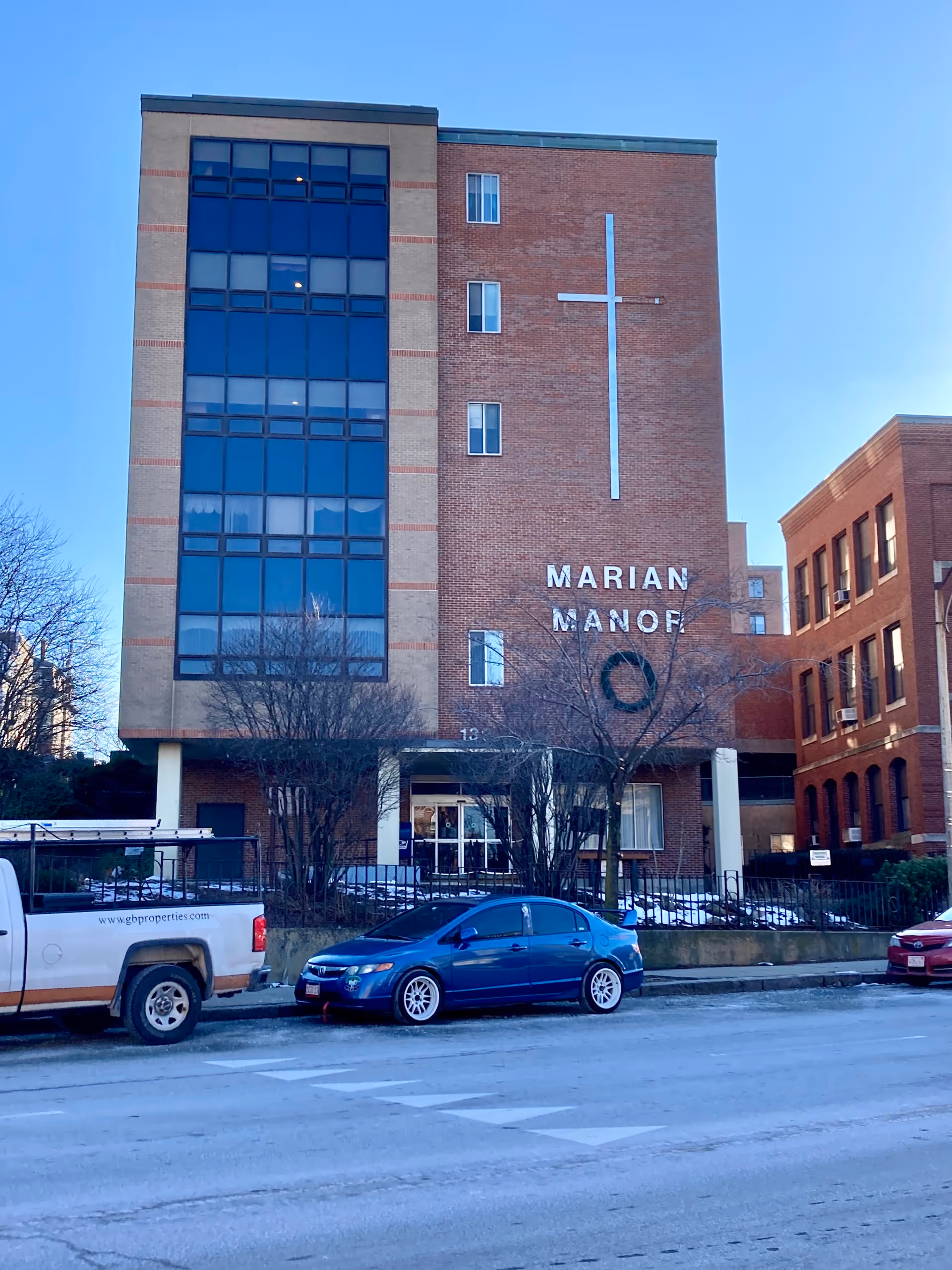 Exterior view of Marian Manor Nursing Home showcasing a brick building with a cross and parking area.