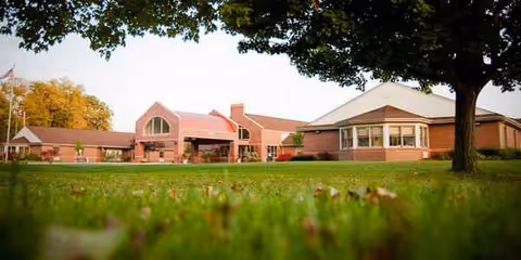 Brick senior care facility exterior with a grassy lawn and trees.