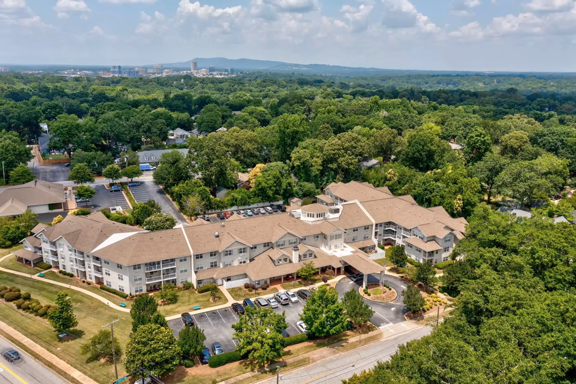 Aerial view of a multi-wing senior living building with a covered entrance, parking lots, and surrounding trees.