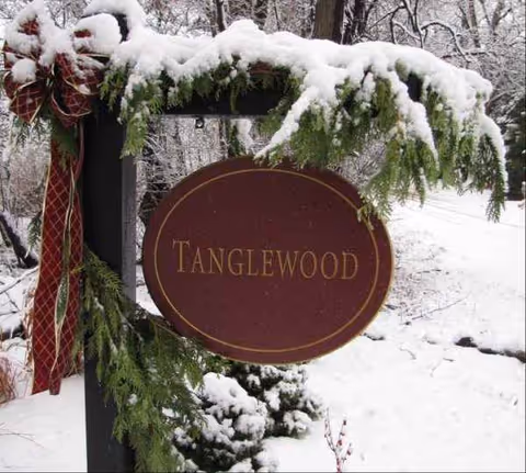 Snow-covered Tanglewood sign with evergreen garland and red ribbon at exterior entrance