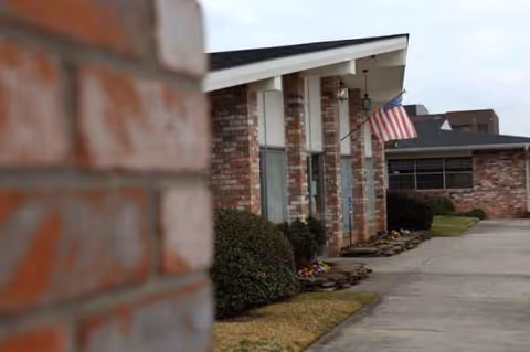 Exterior view of Claiborne Healthcare Center, brick building with walkway, shrubs, and an American flag.