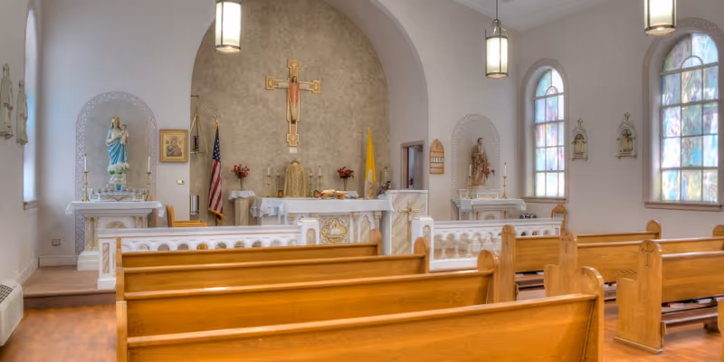 Small chapel interior with wooden pews facing an altar topped by a crucifix and stained-glass windows.