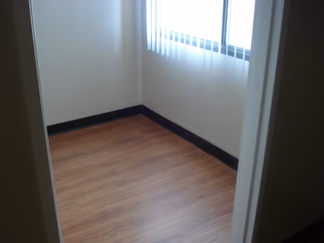 Empty room with wood flooring, white walls, a window with vertical blinds, and black baseboards.
