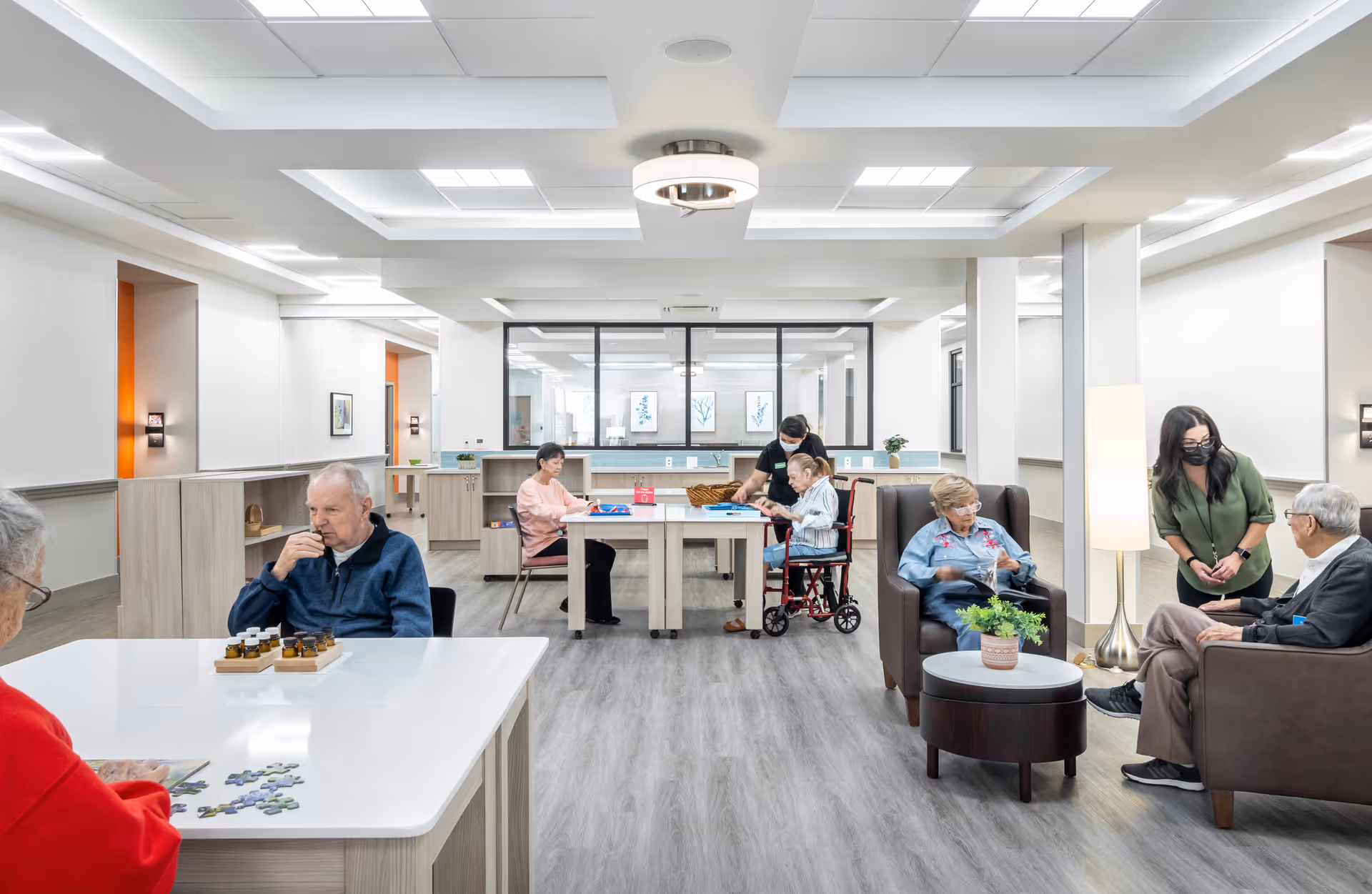 Bright communal activity lounge in a senior living facility with residents and staff interacting.