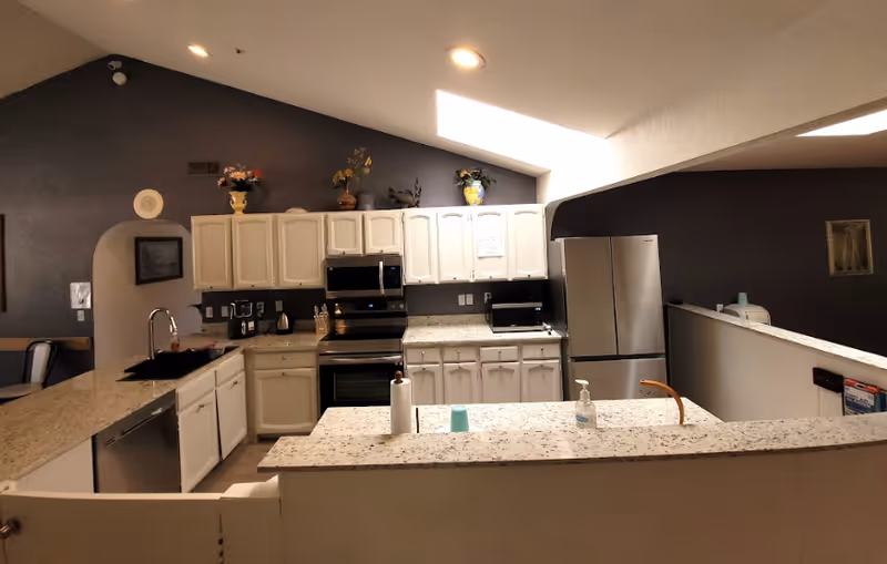 Open kitchen with white cabinets, speckled granite countertops, stainless-steel appliances, and a sloped skylight.