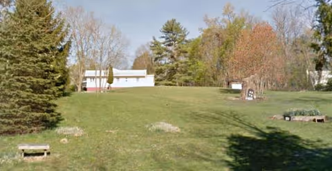 Spacious grassy lawn with a distant white building and trees in a peaceful outdoor setting.