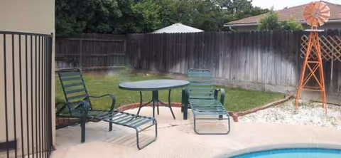 Outdoor backyard patio with a round table, green chairs, fence, and a wind spinner.