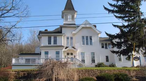 White multi-story building with a central tower and front stairs, set among trees