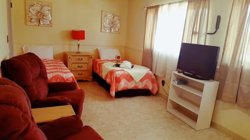 Two twin beds with red quilts, a burgundy sofa, and a TV in a shared bedroom.