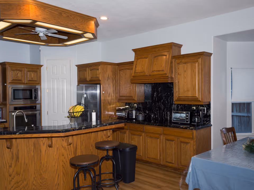 Spacious kitchen with wooden cabinets, black granite countertops, an island with barstools, and stainless steel appliances.