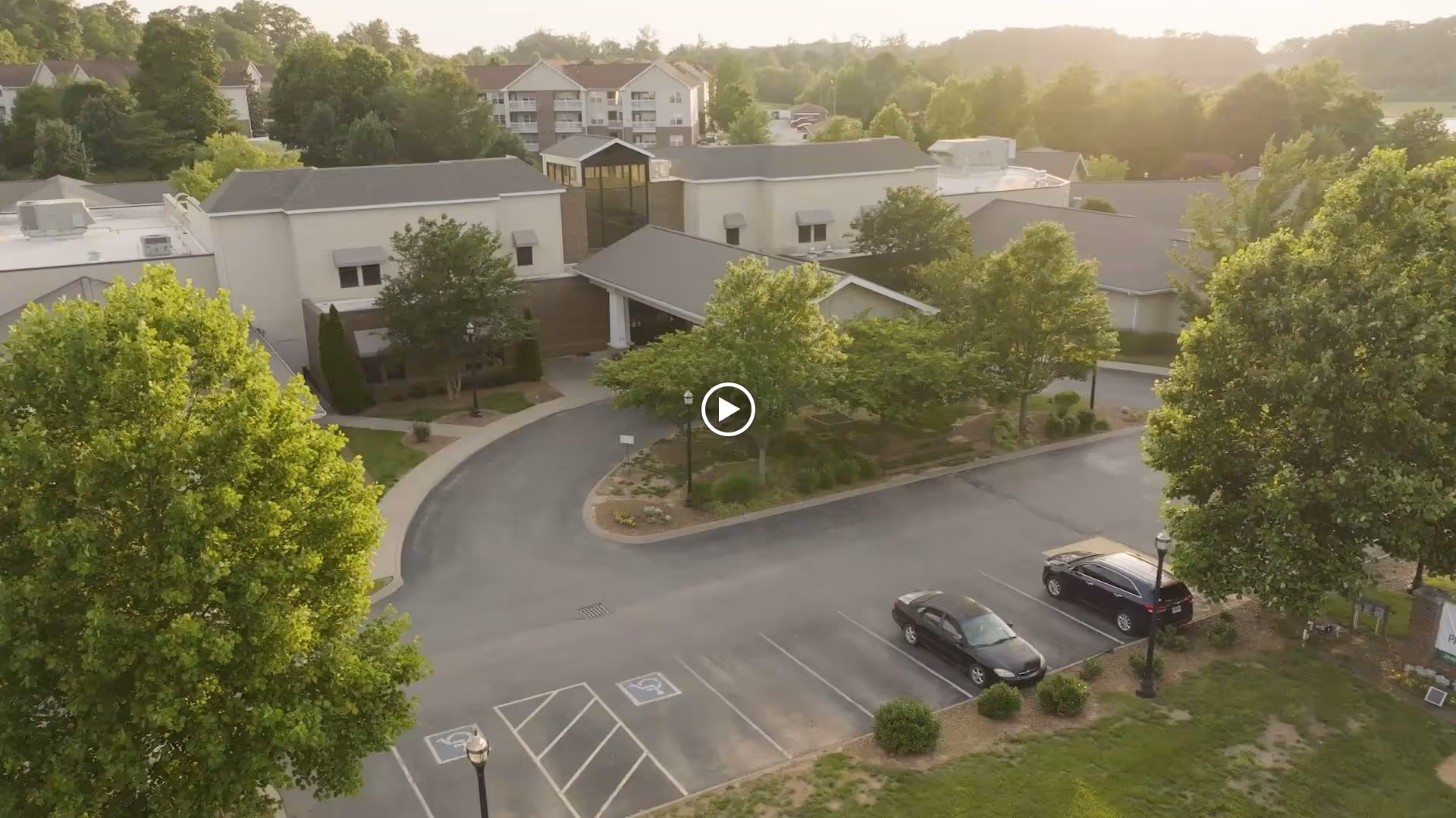 Aerial view of the front entrance and parking lot of a senior living facility surrounded by trees.