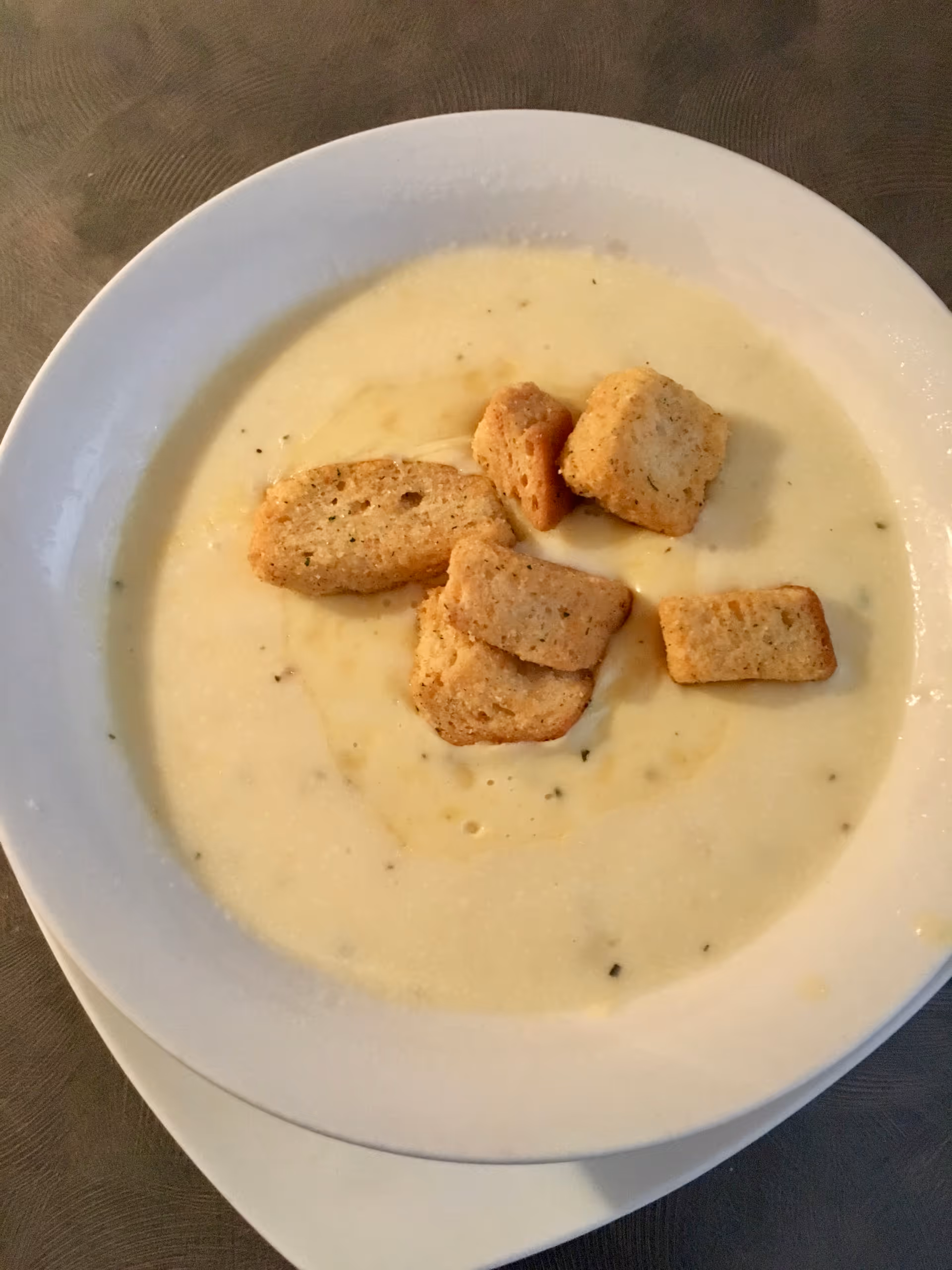A bowl of creamy soup topped with several croutons, served on a white plate with a napkin underneath.