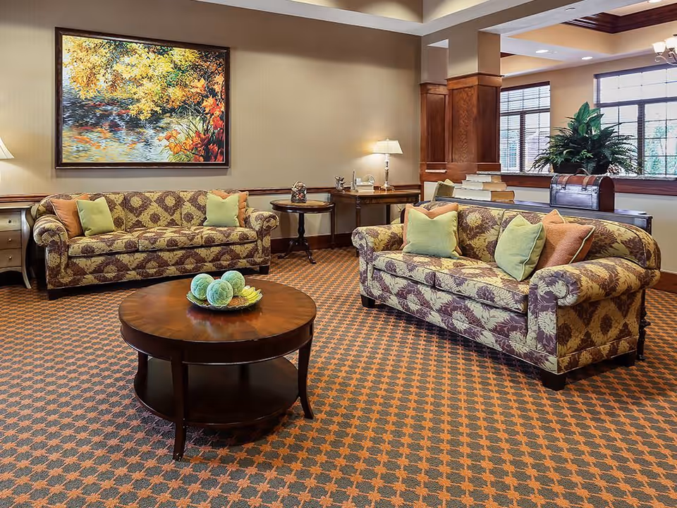 A warm communal lounge with two patterned sofas, a round wooden coffee table, decorative pillows, and a large painting on the wall.