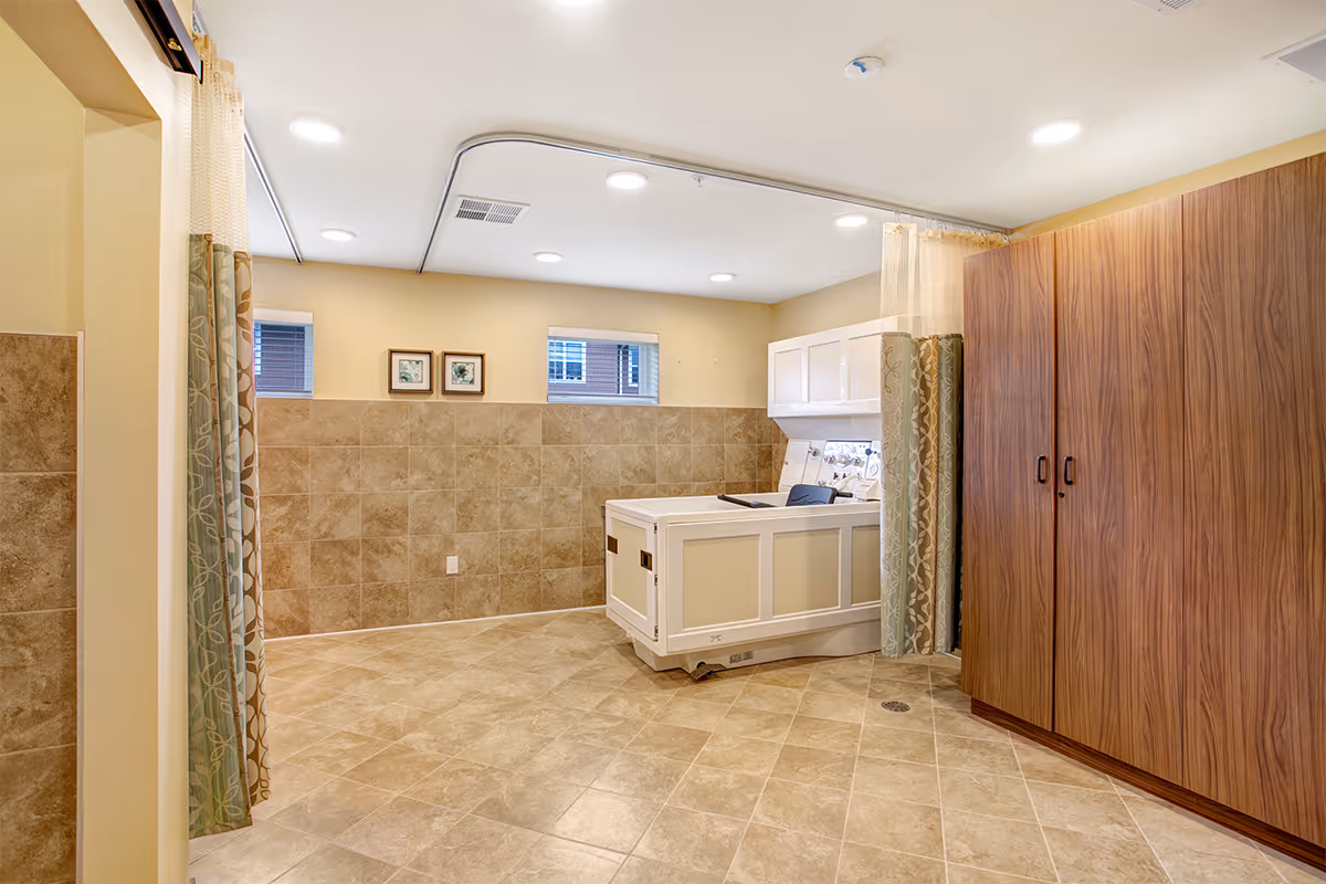 Spacious tiled bathing room with a walk-in tub, ceiling-mounted privacy curtains, and wooden storage cabinets.