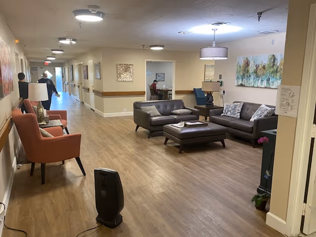 Wide interior hallway in a senior living facility with a seating area of sofas, chairs, and lamps.