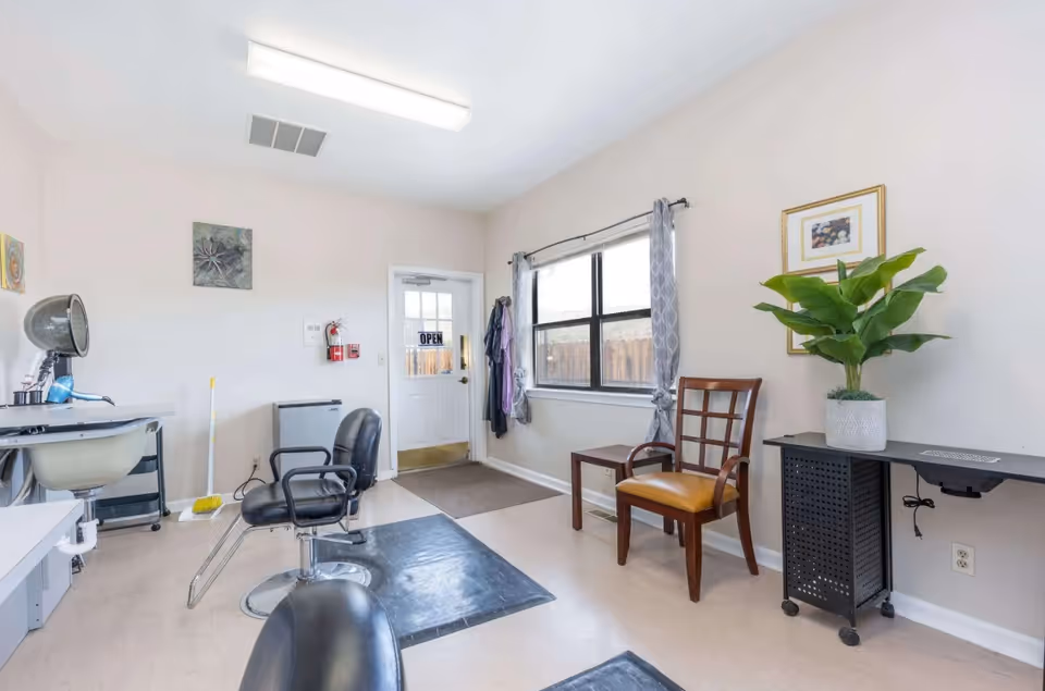 Small interior salon area with styling chairs, a hooded hair dryer, a potted plant, window and a door with an "OPEN" sign.